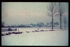 Een besneeuwd landschap met achteraan enkele boerderijen.