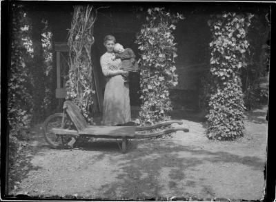 Marguerite Boone met een zoon Caron in groentetuin op Boone's Blijk.  Serre achtergrond, kruiwagen voorgrond.